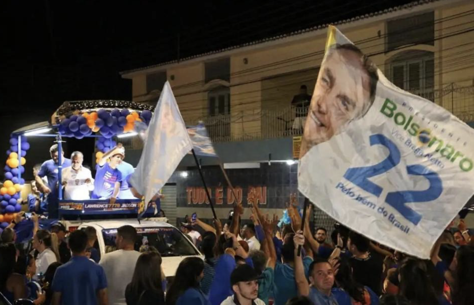 Ato noturno com bandeira de Jair Bolsonaro em primeiro plano